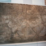 神と怪獣のレリーフ　雷を持った有翼の神が恐ろしい表情をした怪獣を追っている