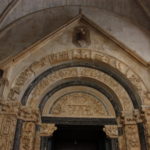 聖ロヴロ大聖堂　門の上のレリーフ、半円形の中心にキリストの誕生、周りの輪には受胎告知やキリストの磔刑の場面が描かれいるようだ